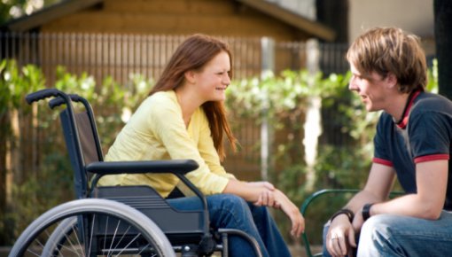 Foto von junger Frau im Rollstuhl im Gespräch mit einem Freund