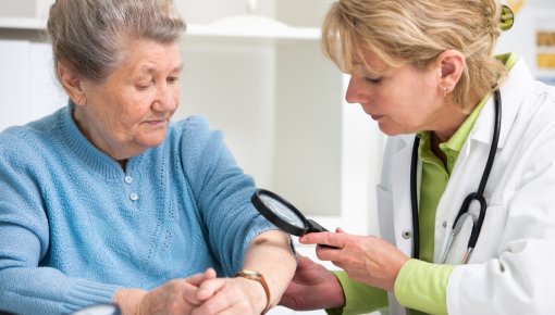 Foto von älterer Patientin und Ärztin bei der Untersuchung auffälliger Hautstellen