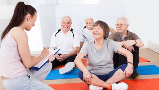 Gruppe von sitzenden älteren Menschen mit Trainerin in Fitnesskurs