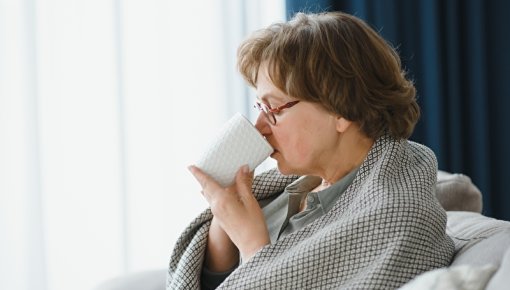 Ältere Dame mit Decke sitzt im Sessel und trinkt eine Tasse Tee