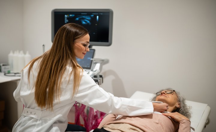 Foto von liegender Patientin, bei der Ärztin ein Ultraschallbild der Halsschlagader macht