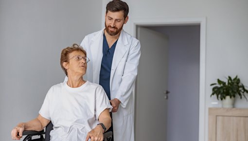 Foto von Patientin im Rollstuhl und Pfleger