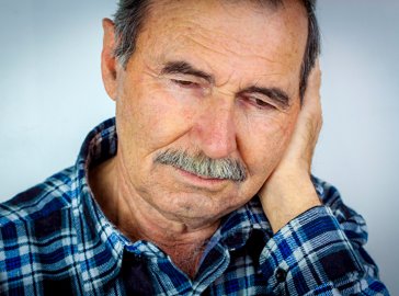 Foto von älterem Mann, der sein linkes Ohr berührt